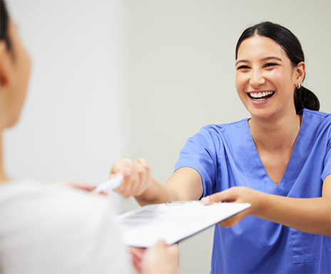 Smiling dental team member handing a clipboard to a patient