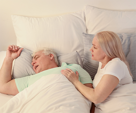 Woman in bed trying to wake up the man sleeping next to her